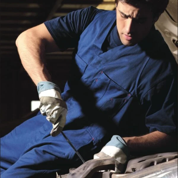 A person wearing a blue work uniform and white gloves is focused on working with tools under the hood of a vehicle. The word BOCINI is at the top left and WORK WEAR is at the bottom. The background is a dimly lit workshop.