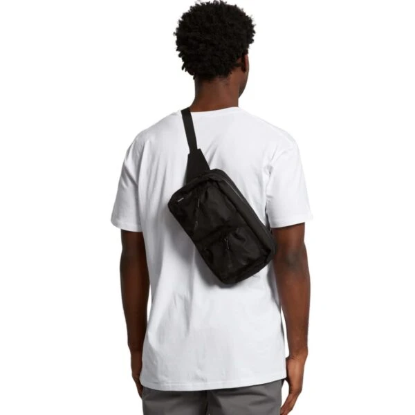 A person with short, curly hair wearing a plain white t-shirt and gray pants is facing away. They have a black crossbody bag slung over their shoulder.