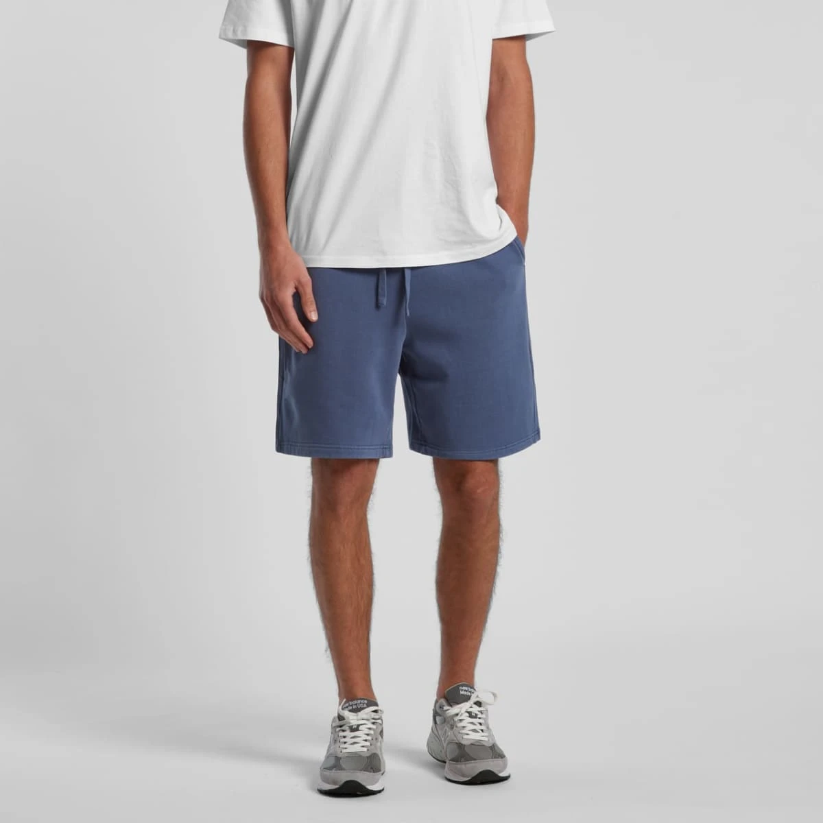 Person in a white t-shirt, blue shorts, and gray sneakers standing against a plain background.