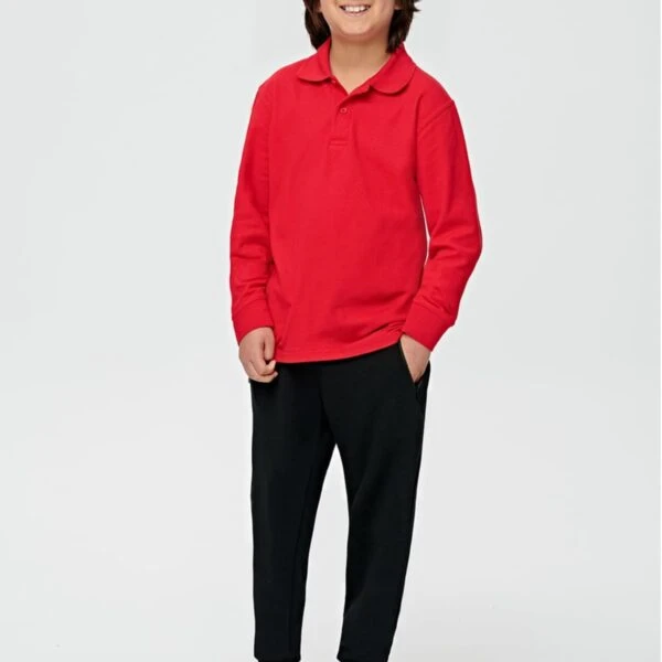 Smiling boy in a red long-sleeve polo and black pants, standing with hands in pockets.
