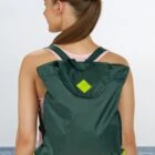 Person with green backpack facing the sea, wearing a pink top.