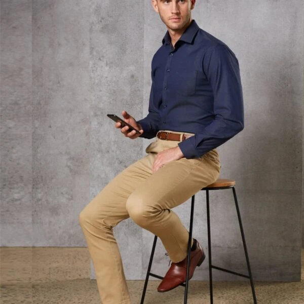 Man in navy shirt and beige pants sits on a stool, holding a smartphone.