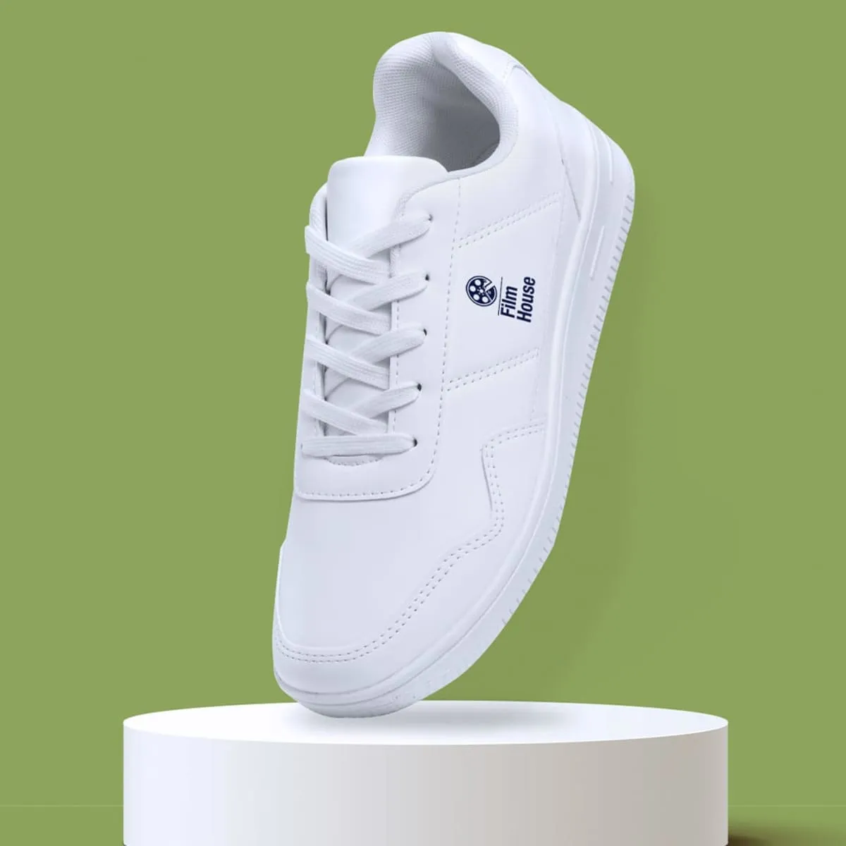 White sneaker with Film House logo, displayed on a round white pedestal, green background.