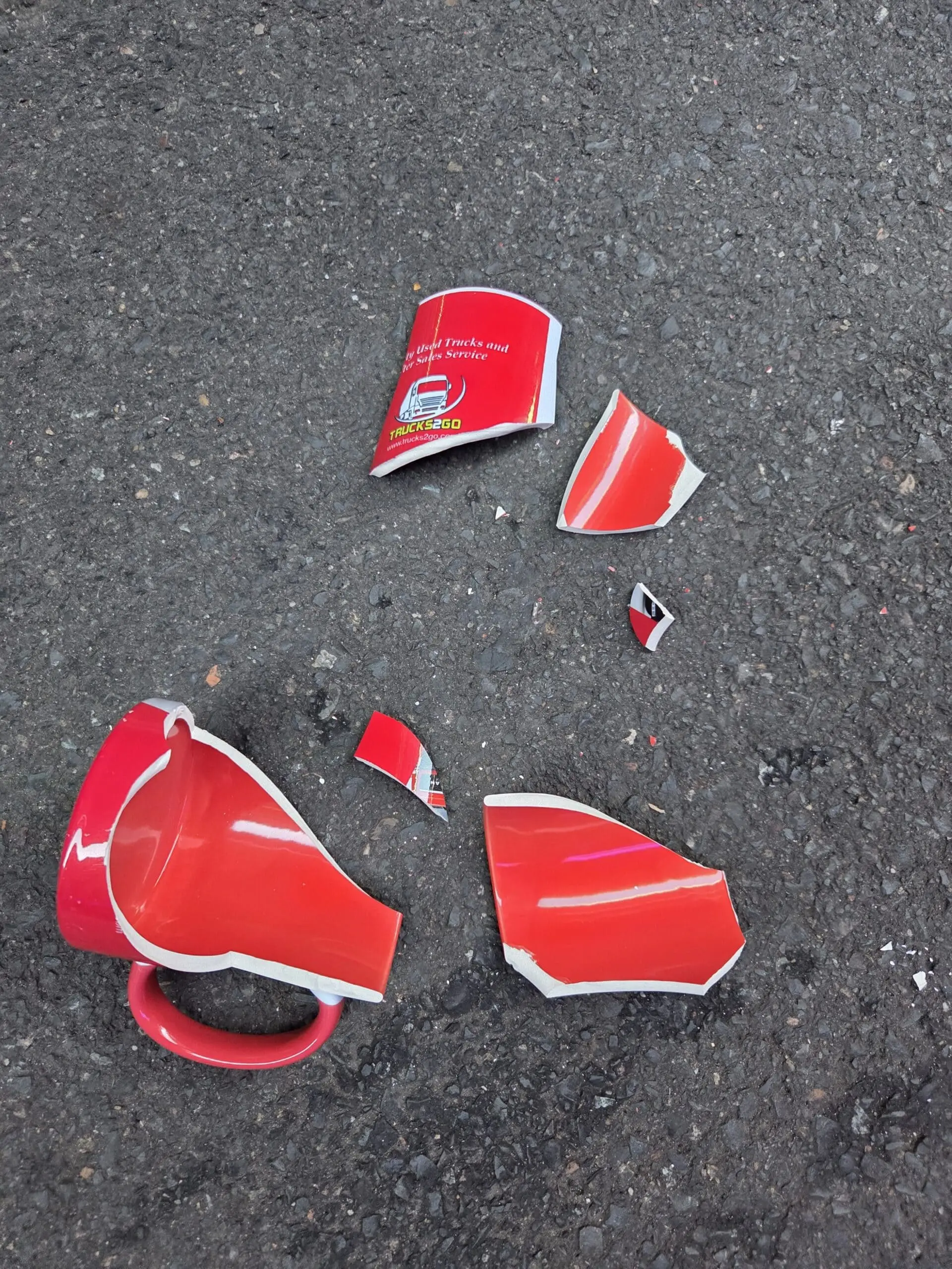 A red ceramic mug, unlike durable porcelain mugs, shattered on a rough gray surface.