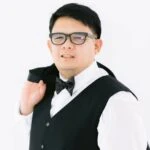 Man in glasses, tuxedo vest, and bow tie, holding his jacket