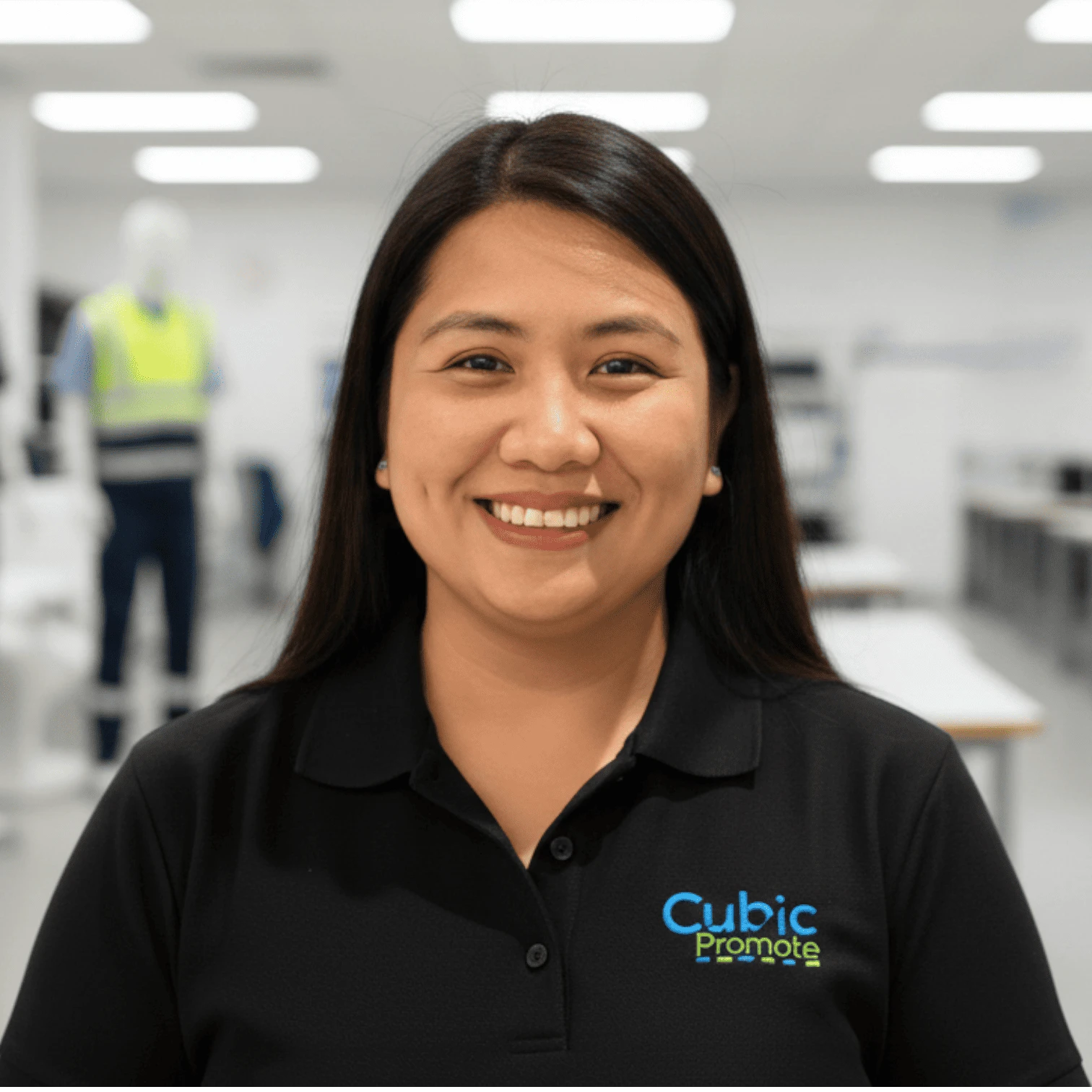Woman smiling in an office, wearing a black Cubic Promote polo shirt—meet the team.