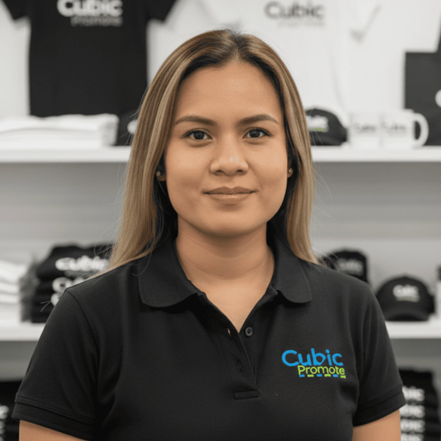 Meet the team: Woman in a black Cubic Promote polo shirt standing among branded merchandise.