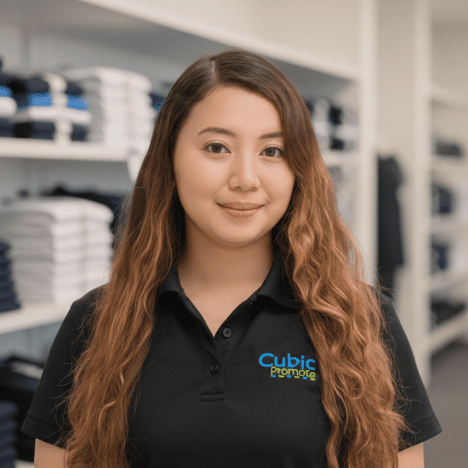 Meet the team: Woman in a black Cubic Promote shirt stands by folded clothes on shelves.