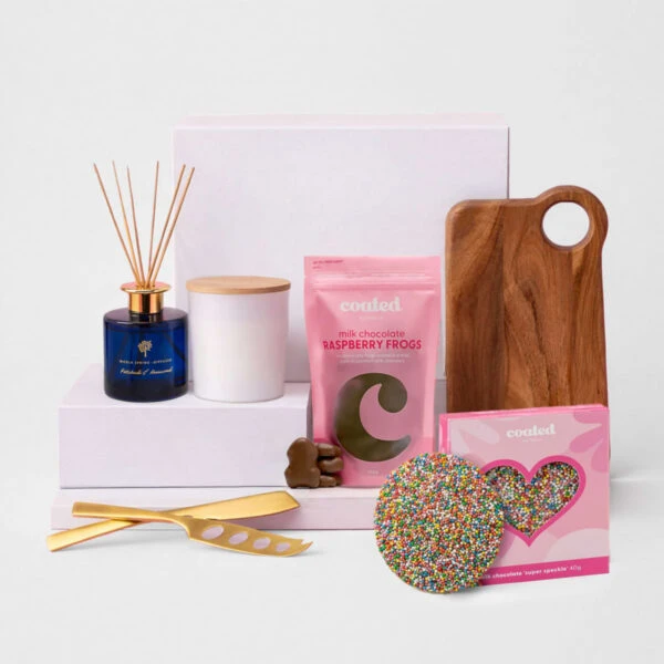 Gift set with candle, diffuser, chocolates, cheese knife, and wooden serving board.